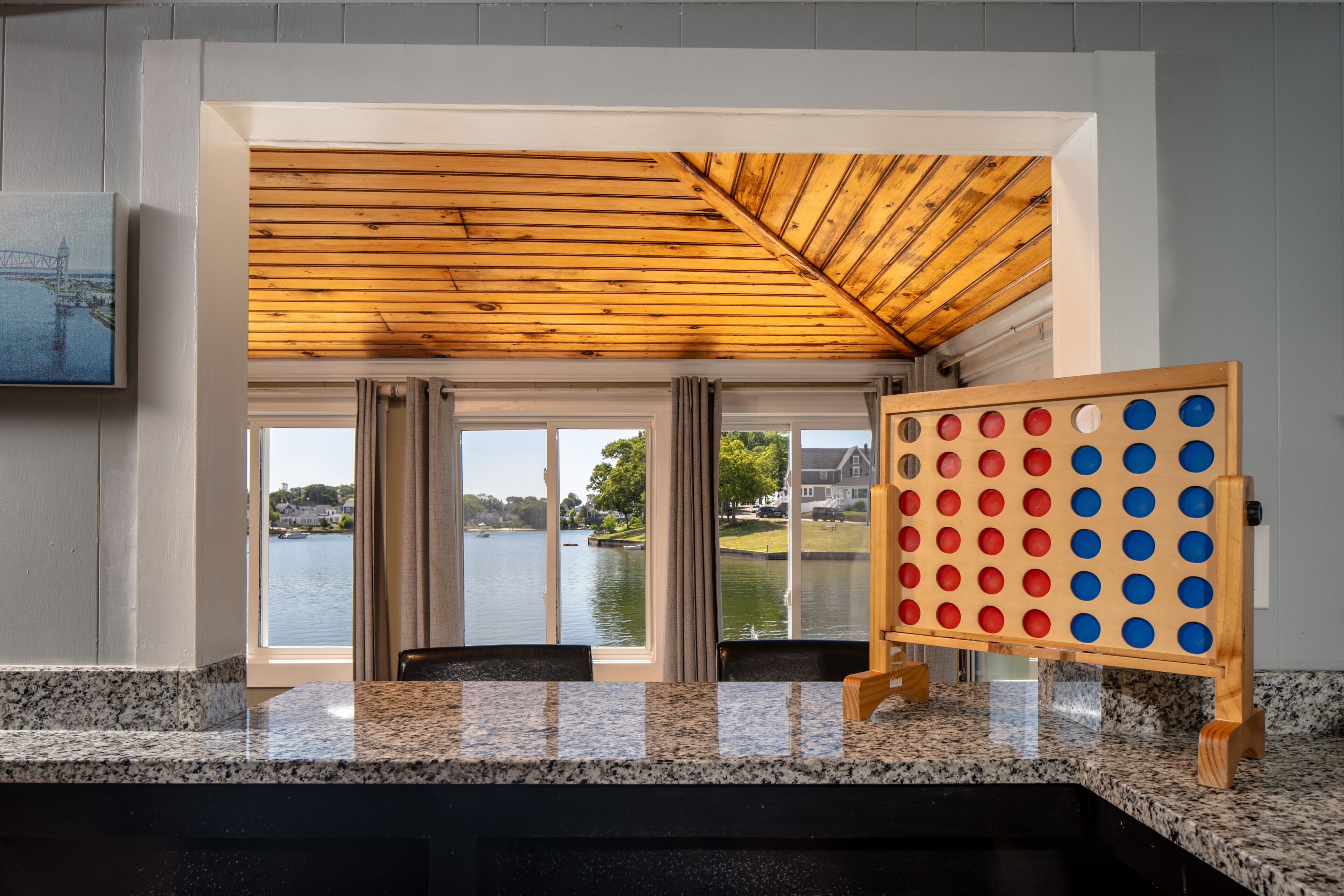 Una cucina con piani di lavoro in granito, soffitto in legno e vista su un lago attraverso ampie finestre.