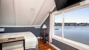 A bedroom with a bed, a small table, a lamp, and a view of a body of water through a large window.
