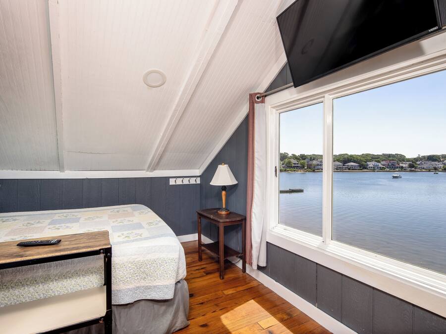 A bedroom with a bed, a small table, a lamp, and a view of a body of water through a large window.