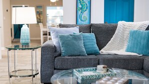 Un salon avec un canapé gris, une table basse en verre et une lampe posée sur une petite table d’appoint.