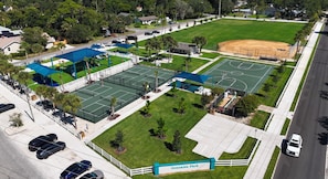 An aerial view of a park with multiple sports courts, a baseball field, and a parking area.