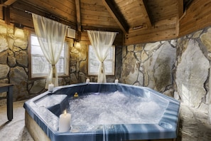 A stone-walled room with a hot tub, candles, and curtains. - Size Matters Cabin! Indoor Hot Tub, Indoor Fire place... (Blue Ridge)