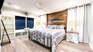 A bedroom with a bed, a ceiling fan, a nightstand, a dresser, a window with curtains, and a wall-mounted fish decoration.