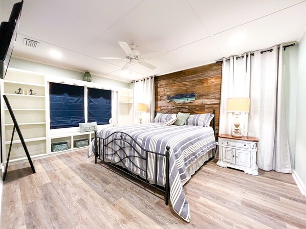 A bedroom with a bed, a ceiling fan, a nightstand, a dresser, a window with curtains, and a wall-mounted fish decoration.