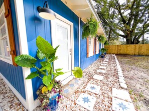 Une maison aux murs extérieurs bleus, avec une porte blanche et un chemin bordé de carreaux en forme d’étoile.