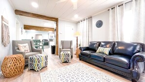 A living room with a black leather sofa, two armchairs, a patterned rug, and a wooden ceiling beam.
