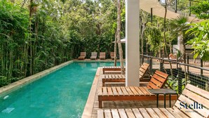 A pool area with wooden loungers and a white column structure. - 3 Story Home with Private Roof Pool and Tropical Views (Tulum)