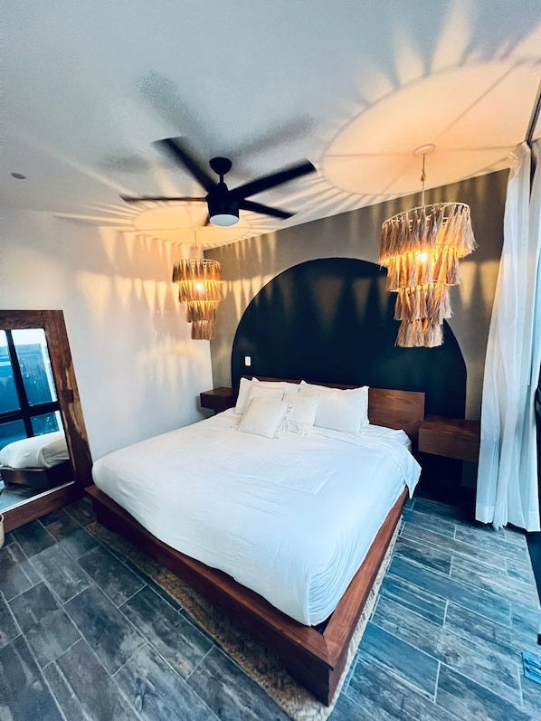 A modern bedroom with a large bed, a ceiling fan, and two hanging light fixtures. - 3 Story Home with Private Roof Pool and Tropical Views (Tulum)
