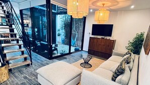 A modern living room with a staircase, a sofa set, a coffee table, and a TV. - 3 Story Home with Private Roof Pool and Tropical Views (Tulum)