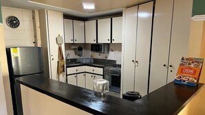 Et køkken med hvide skabe, en sort bordplade, et køleskab, en mikrobølgeovn og en komfur.
