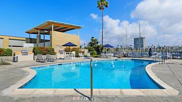 A swimming pool with lounge chairs and umbrellas, a covered barbecue area, and a view of the marina.