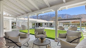 A covered outdoor seating area with a pool, a well-maintained lawn, and a mountain view. - Solaris - Modern Mediterranean Estate with Pool, Spa and Fire Pit (Palm Springs)