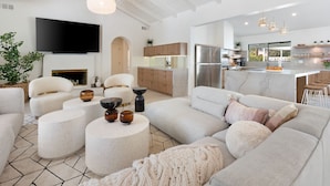A modern living room with a sectional sofa, round coffee tables, and a flat-screen TV. - Solaris - Modern Mediterranean Estate with Pool, Spa and Fire Pit (Palm Springs)