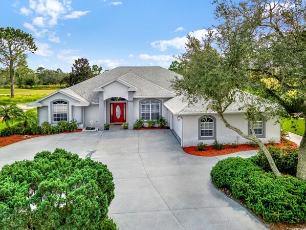 A two-story house with a red front door, a covered front porch, and a driveway leading to the entrance.