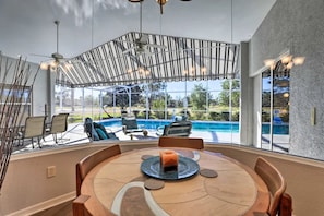 A spacious outdoor dining area with a pool view, a ceiling fan, and a table with a candle centerpiece. - Solar Heated Private Pool & Lanai On Golf Course! (Sebring)