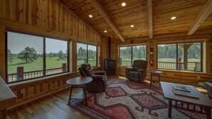 Amplia habitación con grandes ventanales que ofrecen vistas a un paisaje verde. Hay dos sillones de cuero y una pequeña mesa con alfombra.