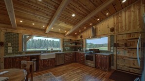 Una cocina rústica con paredes de madera, un ventanal y vista a un bosque.