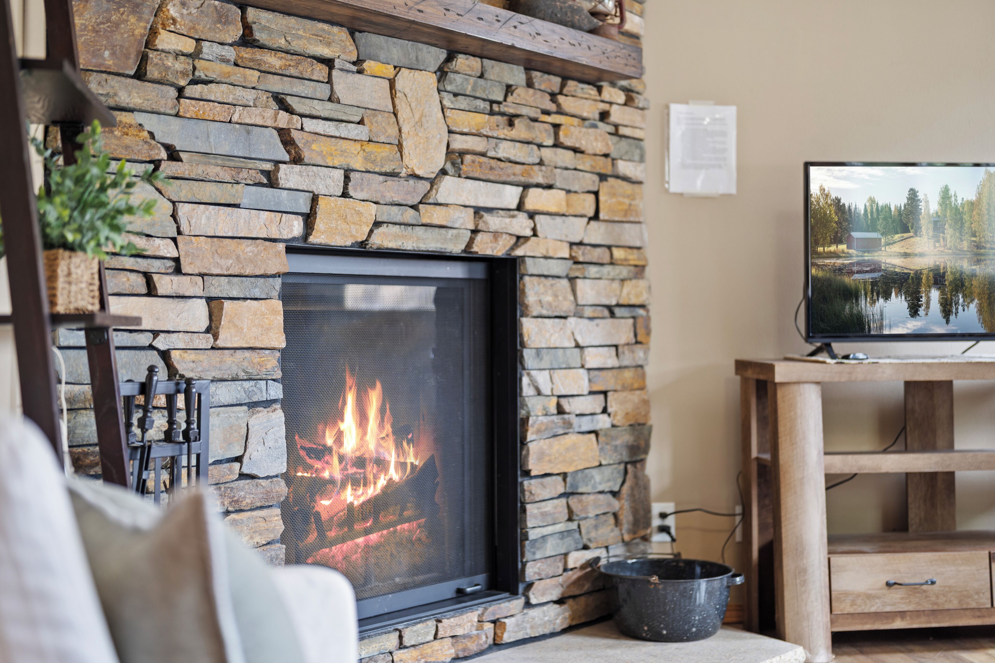 A stone fireplace with a fire, a television on a wooden stand, and a stone wall.