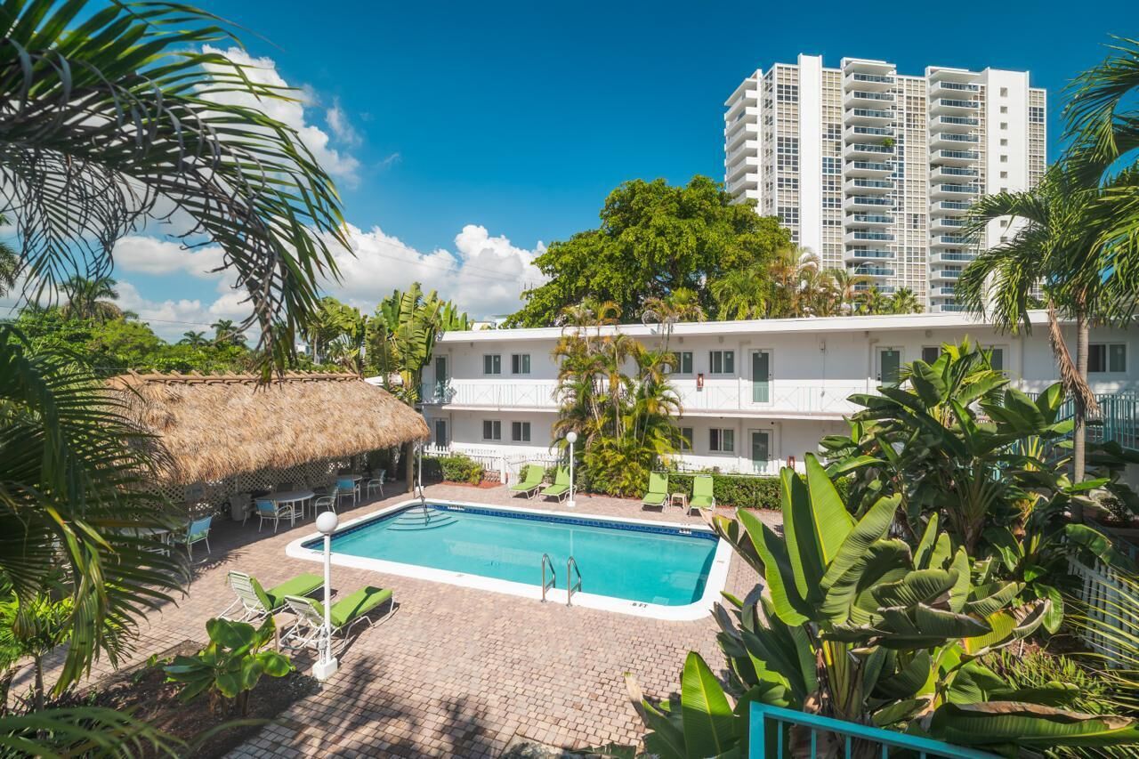 A hotel with a swimming pool, surrounded by lush greenery and palm trees.