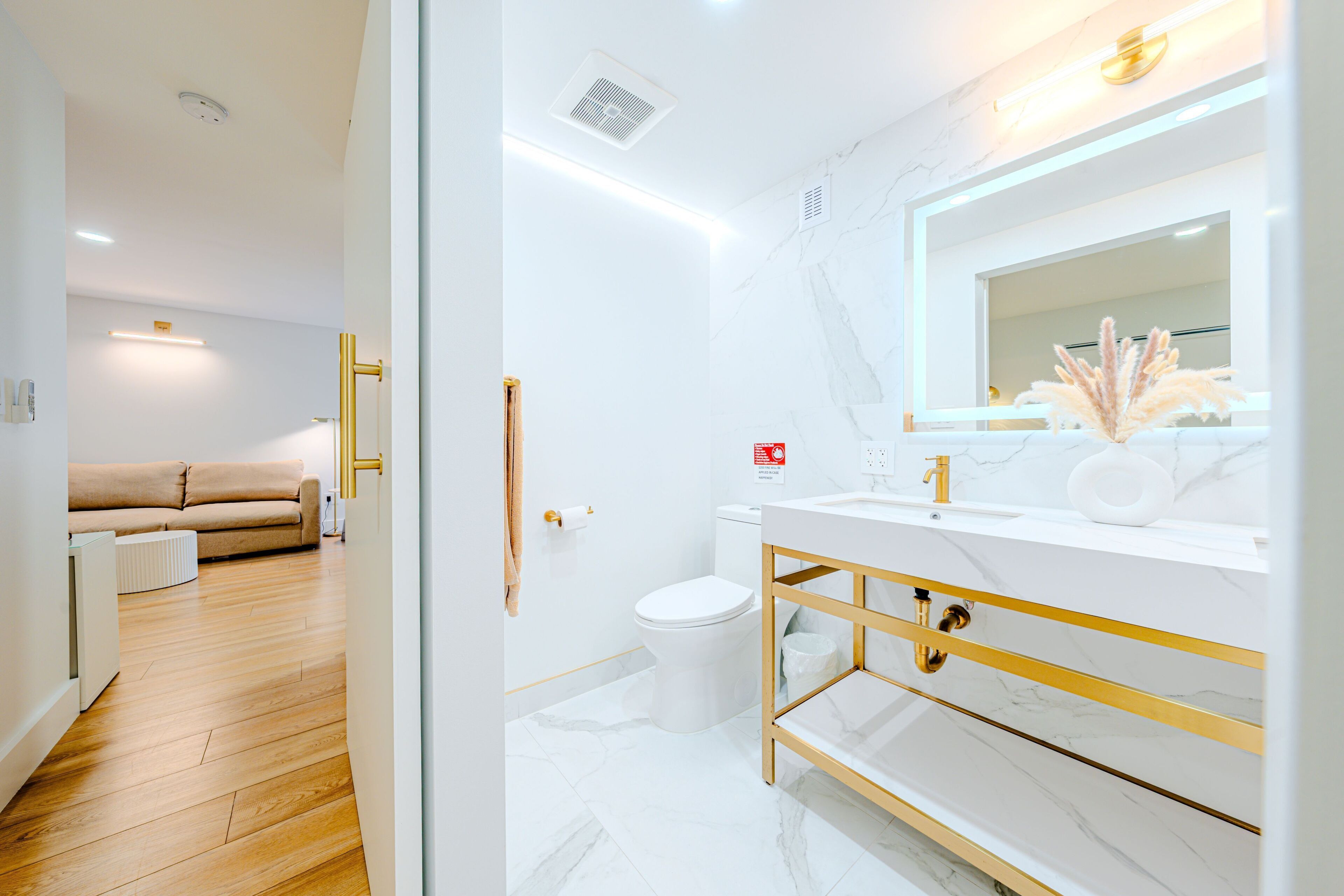 A modern bathroom with a white marble sink, gold fixtures, and a large mirror.