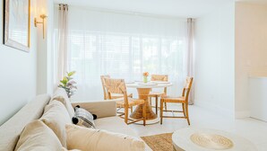 Un salón luminoso con un sofá, una mesa redonda de centro y sillones de mimbre alrededor de una mesa central.