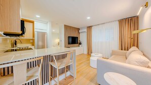 Una cocina moderna con una isla central, un comedor con mesa y sillas blancas, y una sala de estar con sofá y una mesita redonda.