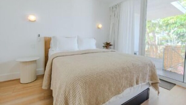Un dormitorio con cama, mesita de noche y ventana con cortinas.