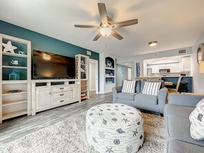 Ein Wohnzimmer mit Fernseher, Deckenventilator, Sofa und einer Küchenzeile.