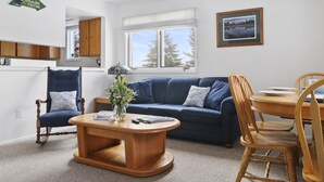 A living room with a blue sofa, wooden dining table, and chairs, a wooden coffee table, and a ceiling fan. - Outpost: Pitchfork 2106 - Walk to Town Square! (Jackson)