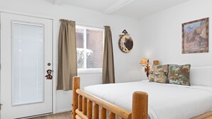 A bedroom with a wooden bed frame, white bedding, a door with a window, and a wall-mounted picture. - Outpost: Pitchfork 2106 - Walk to Town Square! (Jackson)