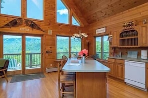 A wooden cabin with a large dining area, a kitchen with wooden cabinets, and a view of the mountains.