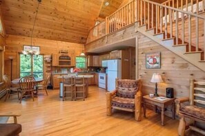 A wooden cabin interior with a kitchen, dining area, and a staircase.