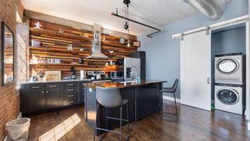Una cucina moderna con rivestimento in legno, un'isola centrale, sgabelli da bar e lavatrice integrata.
