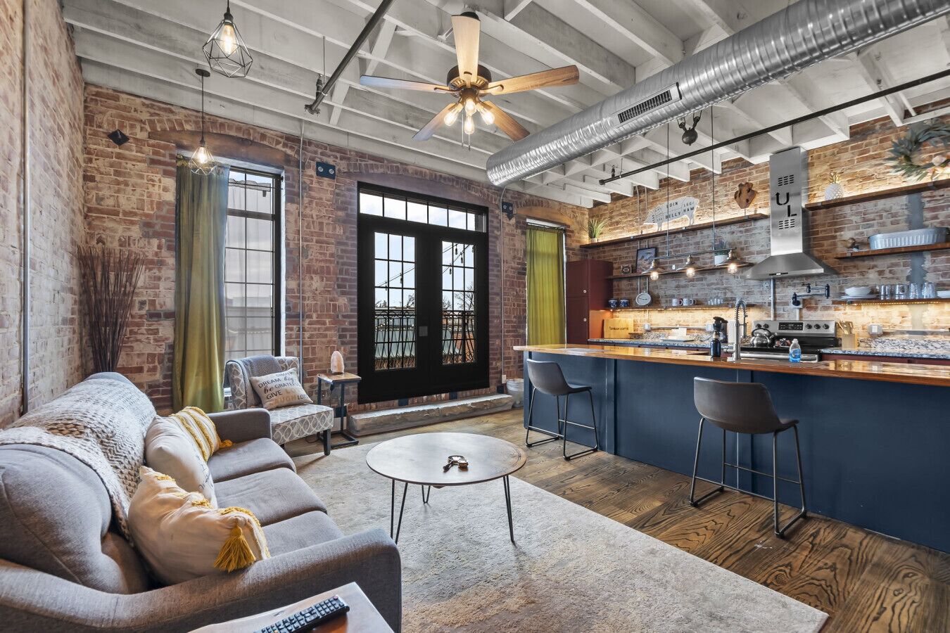 A modern kitchen with a bar area, a dining area with a sofa and chairs, and a large window with curtains.