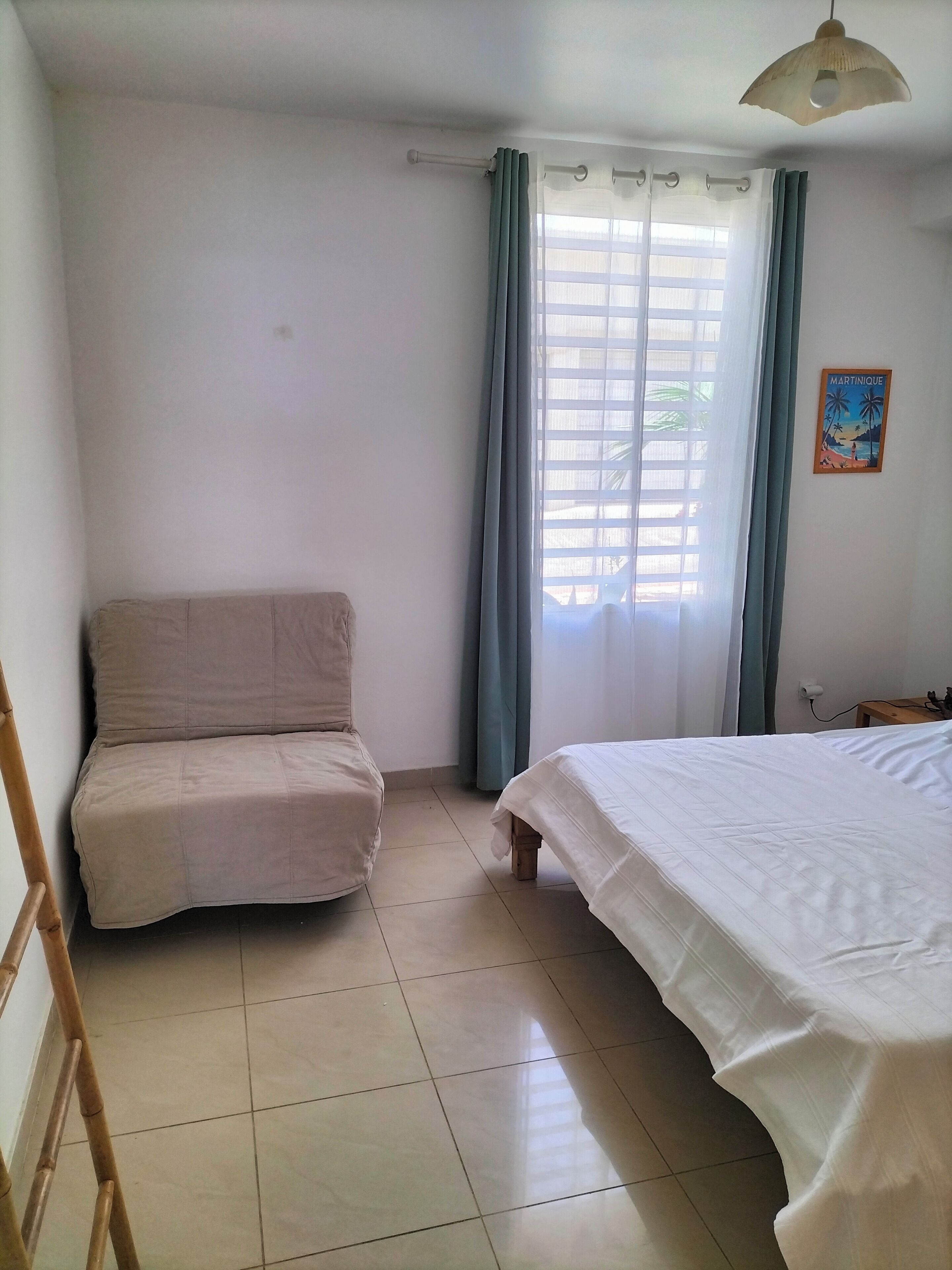 Una habitación con cama, sofá, ventana con cortinas, lámpara de pared y una pequeña mesa.