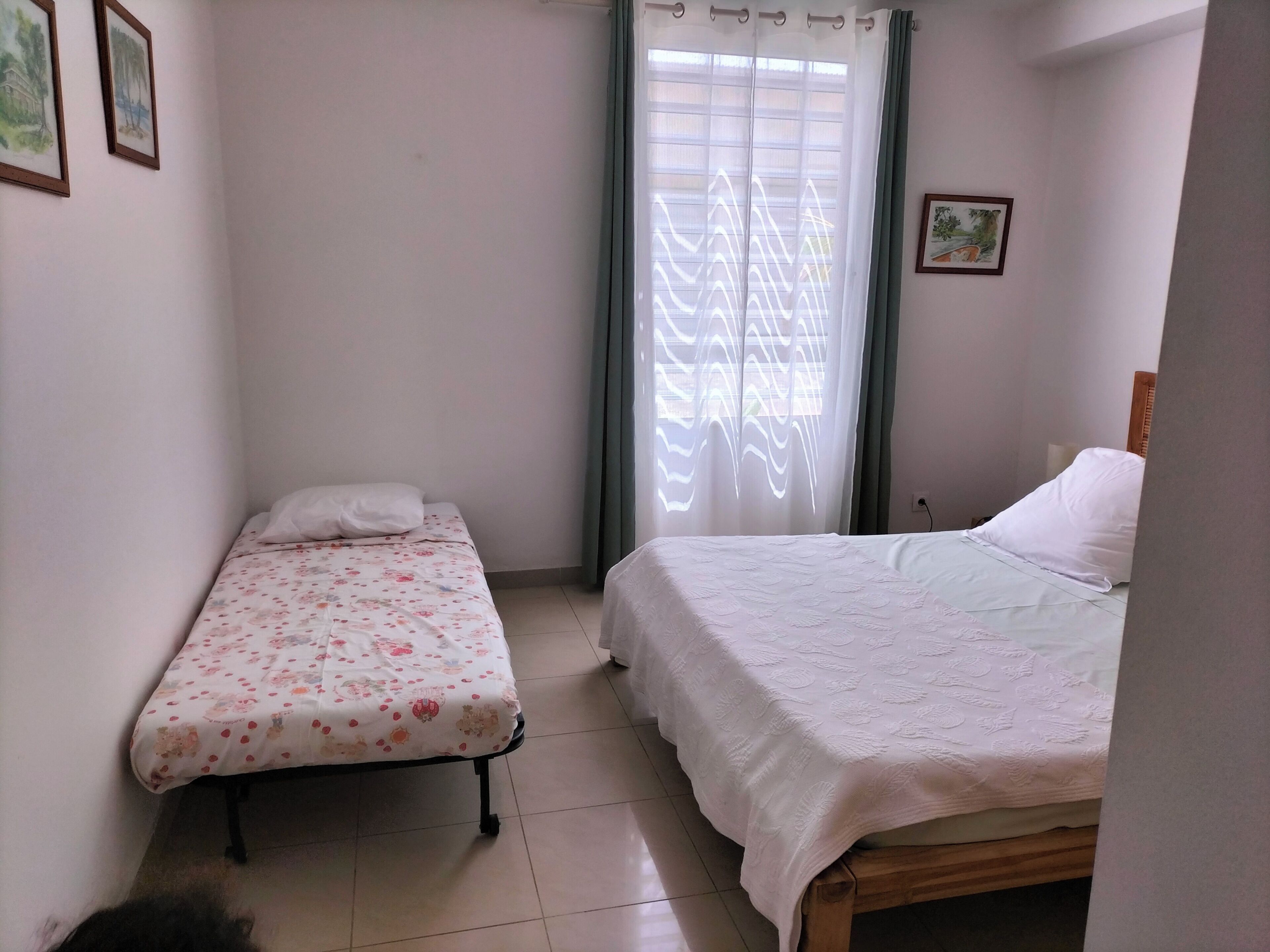 A small, clean room with two beds, one with a floral bedspread and the other with a plain white bedspread.