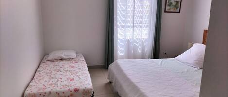 A small, clean room with two beds, one with a floral bedspread and the other with a plain white bedspread.