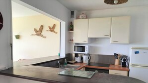 Eine moderne Küche mit weißen Schränken, einer Mikrowelle, einer Kaffeemaschine und einem Toaster. An den Wänden befinden sich Holzdekorationen und ein kleines Regal mit Küchenutensilien.