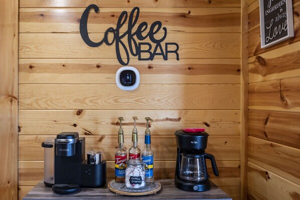 A coffee bar setup with a Keurig machine, a coffee grinder, and three bottles of Torani syrup.