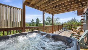 Ein Whirlpool auf einer Holzterrasse mit Blick auf Bäume und Berge.