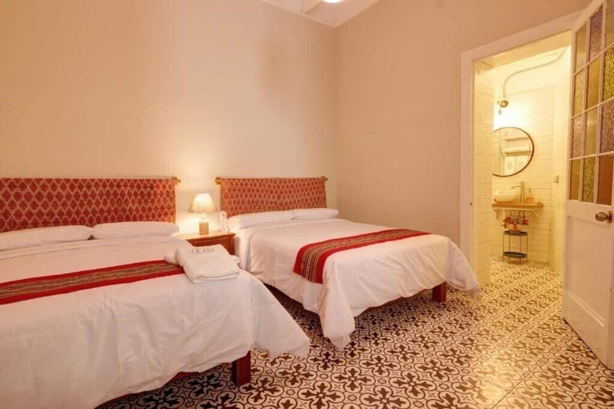 A hotel room with two beds, a patterned floor, and a bathroom with a mirror and sink.