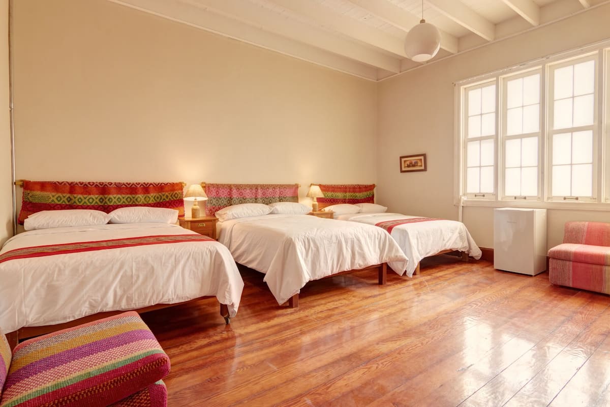 A hotel room with two beds, wooden flooring, a window, and a small refrigerator.