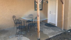A covered patio with a round table and four chairs, a wooden pergola, a white door, and a small window with a green frame. - Casa Colorado: Cozy. Cute. Convenient. (Colorado Springs)