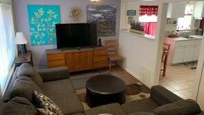 A living room with a sofa, TV, and a ceiling fan. There is a kitchen visible through an open door. - Casa Colorado: Cozy. Cute. Convenient. (Colorado Springs)
