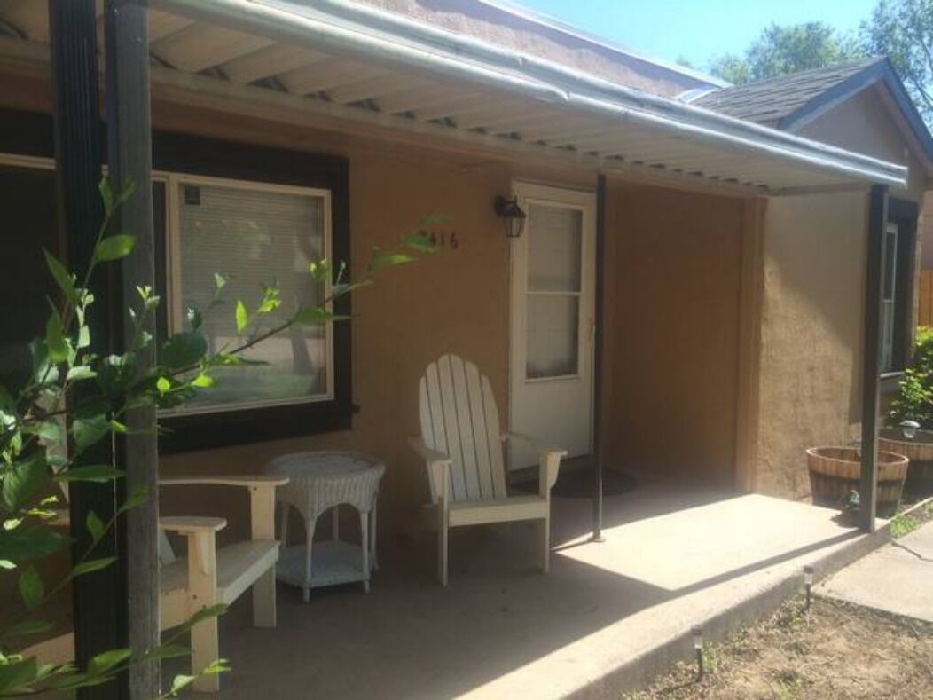 A covered porch with a chair and table, a door, and a window.