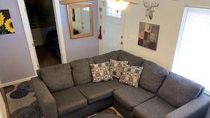 A grey sectional sofa with patterned cushions, a black ottoman, and a decorative mirror on the wall. - Casa Colorado: Cozy. Cute. Convenient. (Colorado Springs)