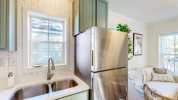 Cocina compacta con refrigerador de acero inoxidable, pileta doble y ventana con persianas.