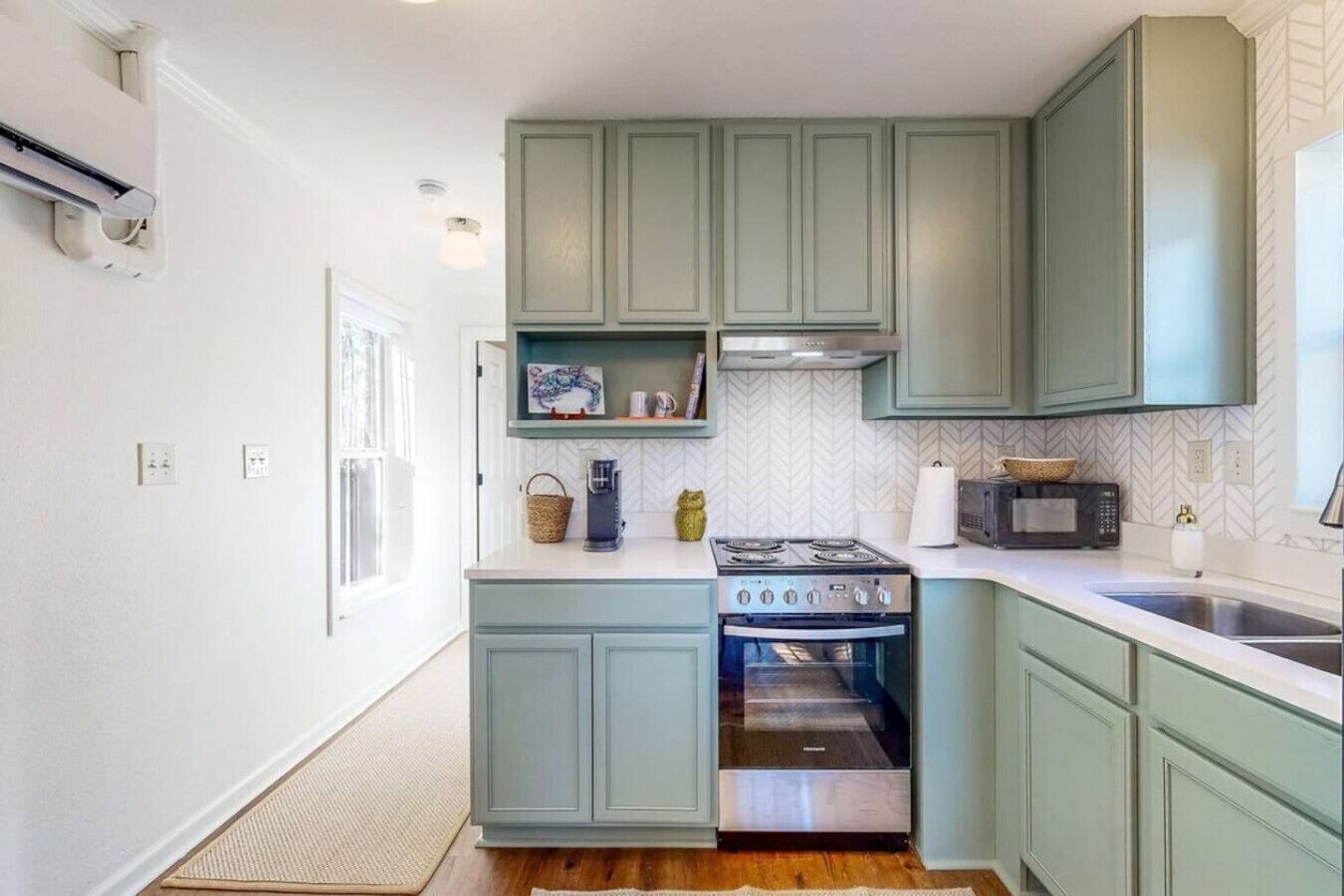 Una cocina compacta con armarios verde claro, horno empotrado, microondas y cafetera sobre la encimera.