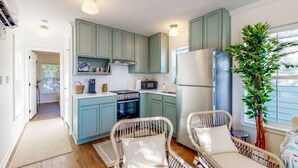 A compact kitchen with teal cabinets, a stainless steel refrigerator, and a microwave. There are wicker chairs and a potted plant. - Picture book cottage! (Ocean Springs)