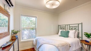 A bedroom with a bed, a window, a bedside table, and a wall-mounted air conditioner. - Picture book cottage! (Ocean Springs)